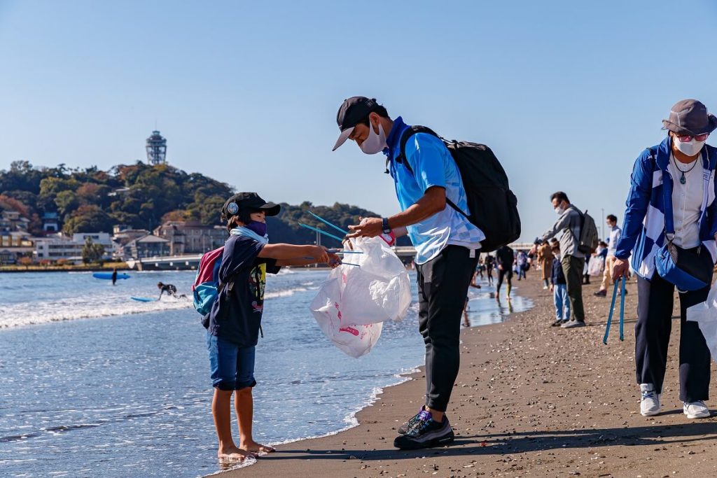 海岸で親子がゴミ拾いボランティアを行う様子の写真
