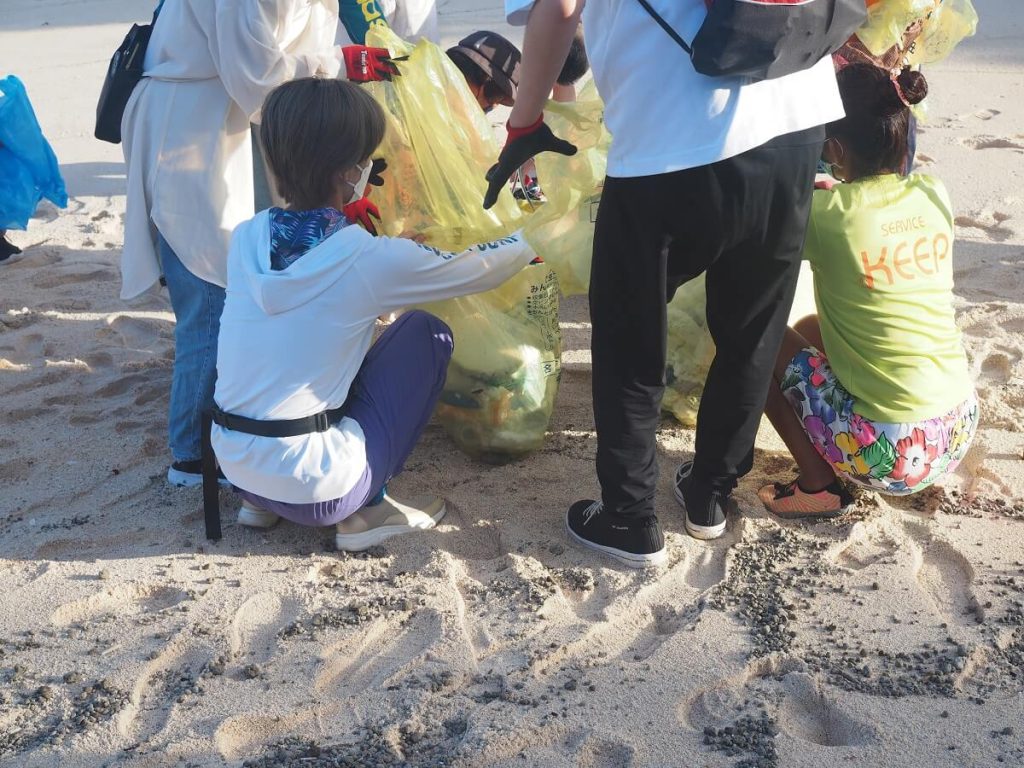海でボランティアたちが黄色いゴミ袋にゴミを集めている様子の写真