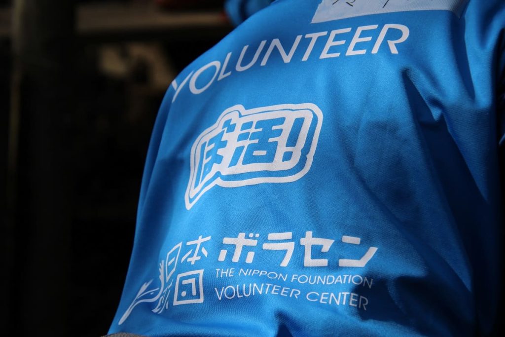 「ぼ活！」のロゴマークが入っているTシャツを着て災害ボランティア活動を行う様子の写真"