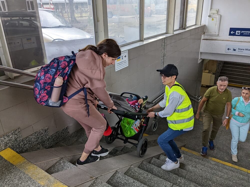 階段でベビーカーを運ぶ女性とボランティアの男性