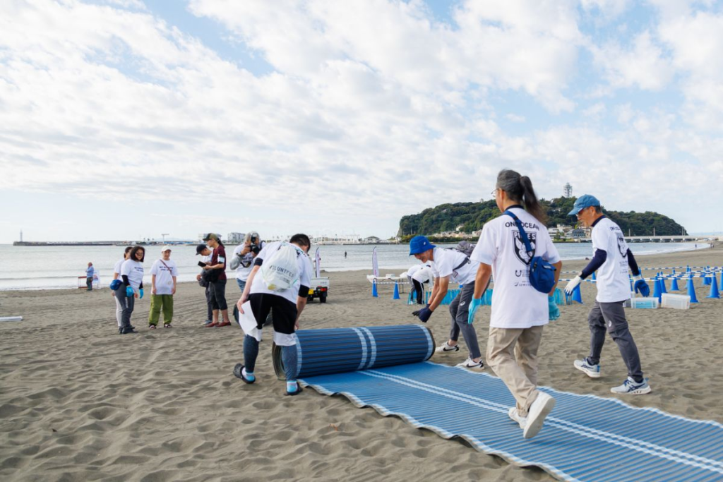 江ノ島を背景に、ボランティアの方達がビーチマットで道をつくる