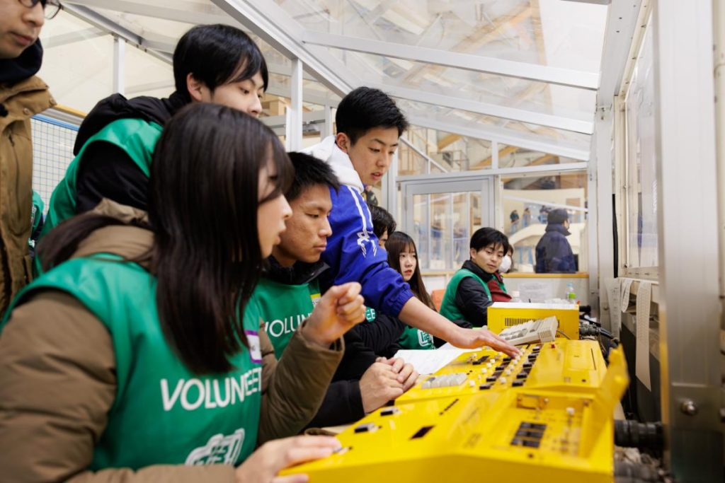アイスホッケーの試合中、軽井沢高校のアイスホッケー部の生徒が機械の操作をする様子を眺めるボランティアたち