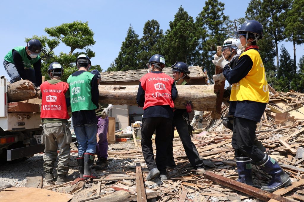 地震の被災地で倒壊した家屋の梁を運ぶボランティアたちの様子