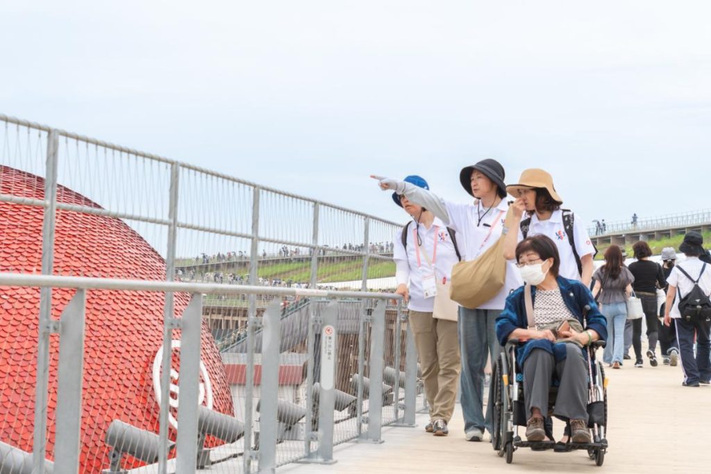 大屋根リングを移動する介護知識のあるLET’S EXPOの会場内サポートボランティアと車いすユーザー