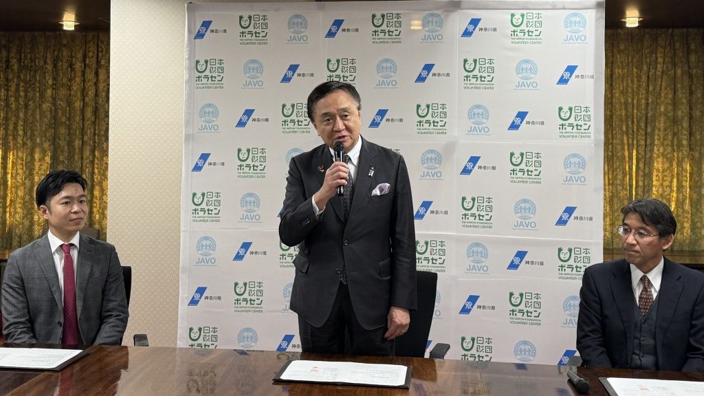 3人の男性がおり、中央の男性が立って話している。
左から、小茂鳥 雅史 JAPANボランティア協会理事長、黒岩 祐治 神奈川県知事、松井 秀彦 日本財団ボランティアセンター専務理事